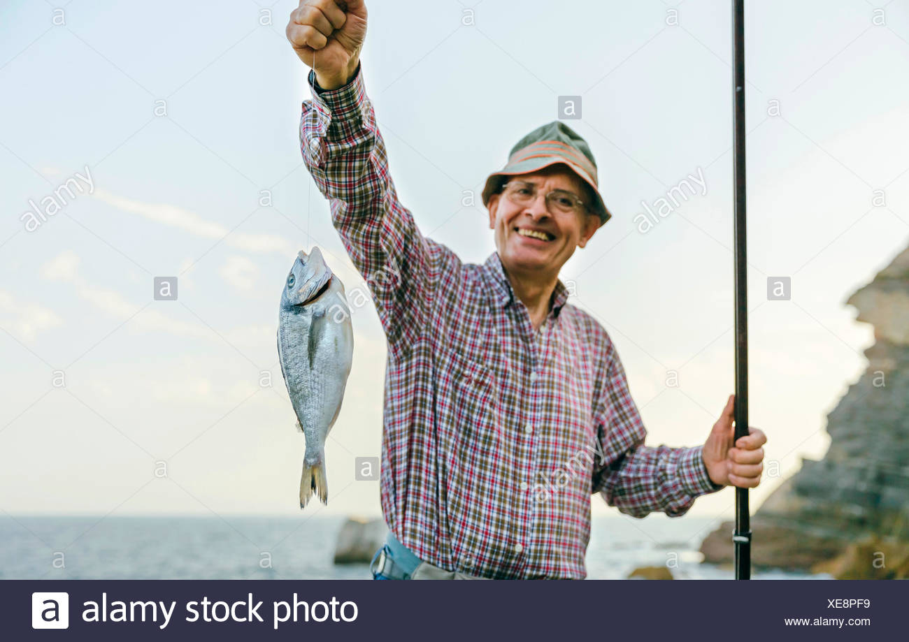 happy-senior-man-holding-fish-on-fishing-line-XE8PF9.jpg